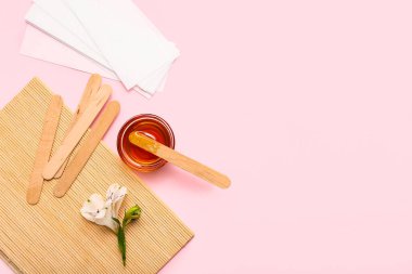 Cam kase şekerli, balmumu şeritli, tahta çubuklu ve pembe arka planda alstromerya çiçekli.