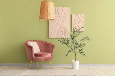 Pink armchair and olive tree near green wall