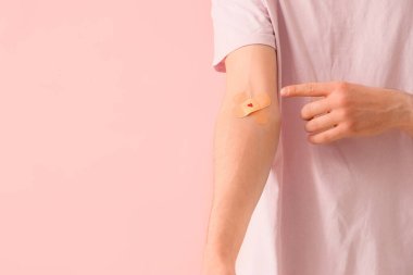 Male blood donor pointing at applied patches on pink background, closeup