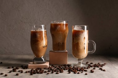 Decorative podiums with glasses of iced latte and coffee beans on grey background