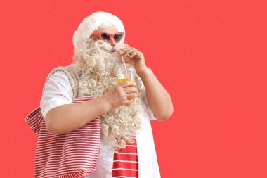 Santa Claus drinking cocktail on red background. Christmas in July