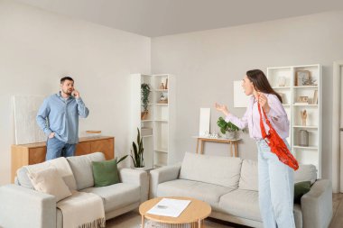 Young man talking by mobile phone and his wife with found mistress's underwear at home. Cheating concept