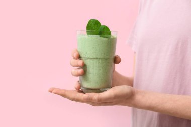 Woman with glass of fresh spinach smoothie on pink background