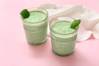 Pembe arka planda bir bardak taze ıspanaklı smoothie.