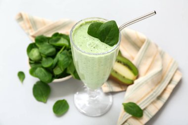 Bir bardak taze ıspanaklı smoothie ve gri arka planda kivi.