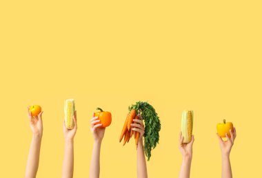 Female hands holding fresh vegetables on yellow background