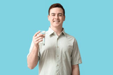 Happy young man with glass of clean water on blue background