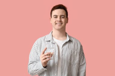 Handsome young man with glass of clean water on pink background