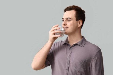 Handsome young man drinking clean water on grey background