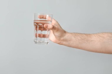 Male hand with glass of clean water on grey background