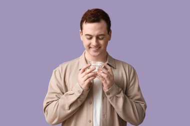 Handsome young man with glass of clean water on lilac background