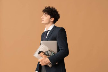 Handsome young businessman with modern laptop and magazine on brown background