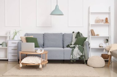 Modern interior of living room with grey sofa and laptop on table