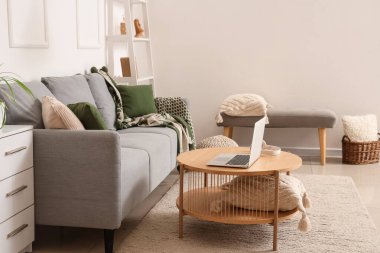 Modern interior of living room with grey sofa and laptop on table