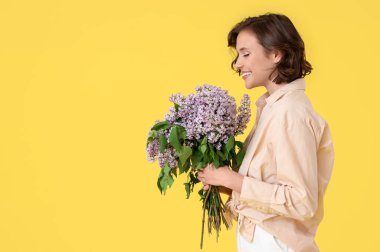 Beautiful young woman with bouquet of blooming lilac flowers on yellow background