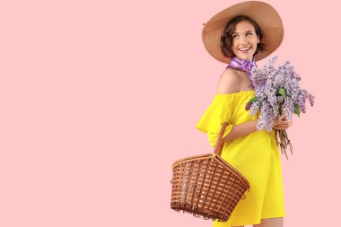 Beautiful young woman with bouquet of blooming lilac flowers and wicker basket on pink background