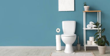 Tuvaletin içinde klozet, raf ünitesi ve mavi duvarın yanında bitkiler var. Tasarım için pankart