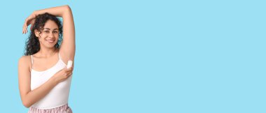 Güzel bir Afro-Amerikalı kadın mavi arka plan üzerine deodorant sürüyor.