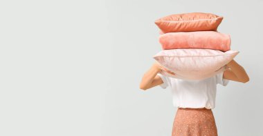 Hafif arkaplanda yumuşak yastıklar tutan bir kadın.