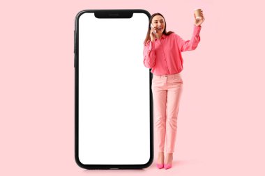 Büyük cep telefonu ve pembe arka planda bir fincan kahvesi olan genç bir iş kadını.