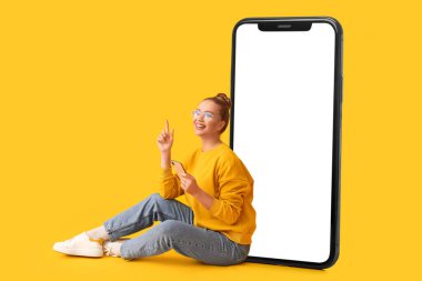 Büyük cep telefonu ve sarı arka planda oturan genç bir kadın.