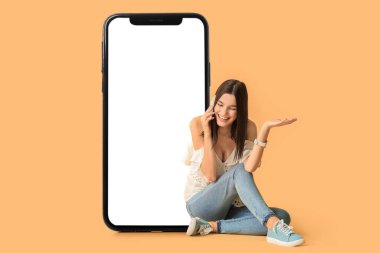 Büyük bir cep telefonu ve bej arka planda oturan genç bir kadın.