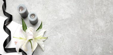 Açık bir kitap, siyah cenaze kurdelesi, yanan mumlar ve arkaplanda nilüfer çiçekleri.