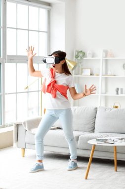 Evde boş gününde VR gözlük takan genç bir kadın.