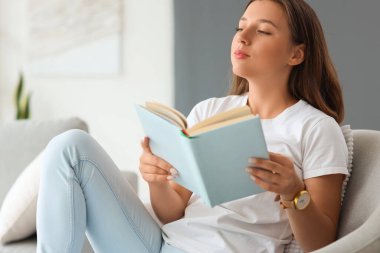 Evde boş gününde kitap okuyan genç bir kadın.