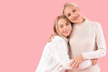 Annesi pembe arka planda sarılırken mutlu ve güzel bir kadın.