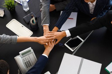 Bir grup iş adamı toplantı salonundaki masada el ele tutuşuyorlar.