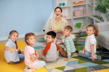 Anaokulundaki küçük çocuklara masal okuyan anaokulu öğretmeni.