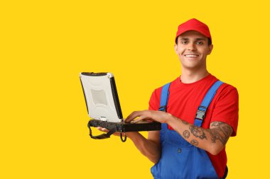 Sarı arka planda dizüstü bilgisayarı olan bir erkek araba tamircisi.