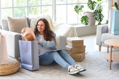 Bilgisayarlı, çantalı ve yeni şapka alışverişi yapan genç bir kadın.