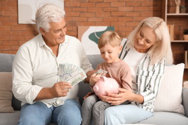 Büyükannesi ve büyükbabasıyla küçük bir çocuk evdeki domuz kumbarasına para koyuyor.