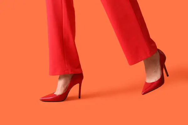 Legs of young woman in stylish red high heels on orange background