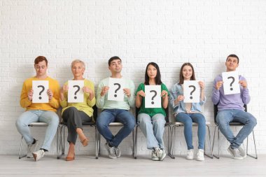 Adaylar beyaz tuğla duvarın yanında soru işaretli kağıt kağıtlar taşıyorlar