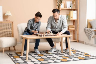 Baba ve küçük oğlu evdeki kanepede satranç oynuyorlar.