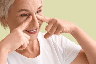 Güzel, olgun bir kadın yeşil arka planda yüz geliştirme egzersizi yapıyor.