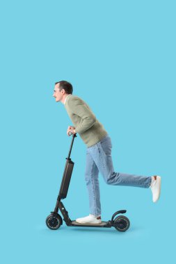 Young man with kick scooter on blue background