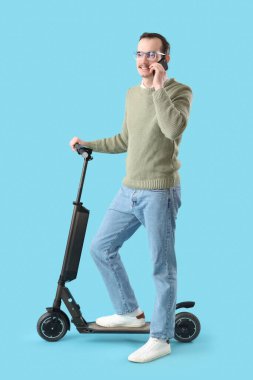 Motorlu genç adam mavi arka planda cep telefonuyla konuşuyor.