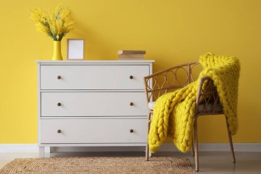 Sarı duvarın yanında koltuk ve örgü battaniyeli dolap.