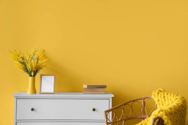 Sarı duvarın yanında koltuk ve örgü battaniyeli dolap.