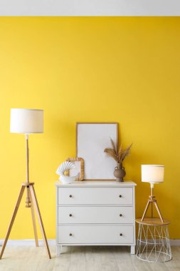 Sarı duvarın yanında lambalar ve çerçeveler olan dolap