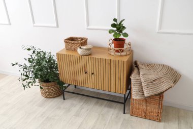 Beyaz duvarın yanında saksıları ve hasır sepetleri olan tahta bir dolap.