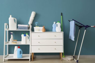 Mavi duvarın yanında temizlik malzemeleri olan bir dolap.