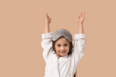 Bej arka planda uyku maskesi takan bornozlu tatlı küçük mutlu kız.