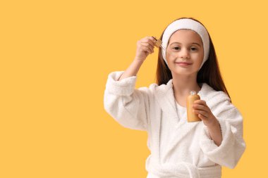 Bornozlu, sarı arka planda bir şişe kozmetik yağı olan tatlı, mutlu bir kız.