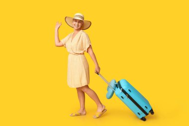 Sarı arka planda bavulu olan olgun bir kadın. Seyahat kavramı
