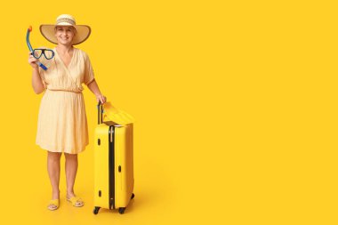 Sarı arka planda şnorkel maskesi ve bavulu olan olgun bir kadın. Seyahat kavramı